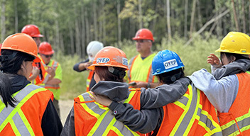 Four youth participants in hardhats and safety vests, huddle on-site